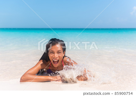 Happy Asian bikini woman laughing playing in splashing wave on Caribbean beach. Summer fun vacation Happy Asian bikini woman laughing playing in splashing wave on Caribbean beach. Summer fun vacation 85900754