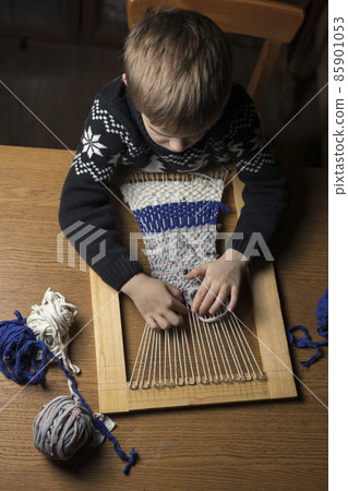 A child weaves a rug made of knitted threads on a homemade loom. Top view. Recycling of old clothes A child weaves a rug made of knitted threads on a homemade loom. Top view. Recycling of old clothes 85901053