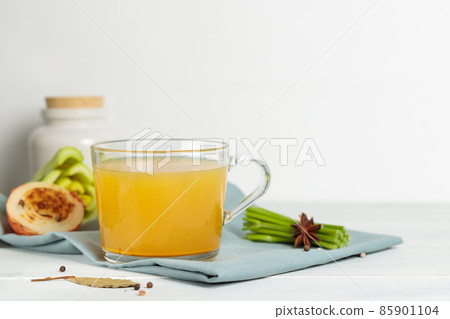 Homemade vegetable or meat broth in a glass mug, on a light background, with baked onions and herbs. Close-up 85901104