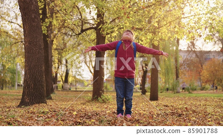 little girl with backpack throws autumn leaves up and laughs, cheerful child plays with leaf fall city street, joyful kid having fun park after school lessons, happy family, children's fantasy dreams 85901788