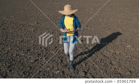 a farmer with a tablet walks on a plowed field of land with a tablet, work on a plantation, farming farming, an agronomist prepares to plant seedlings in organic soil of the land, business production 85901789