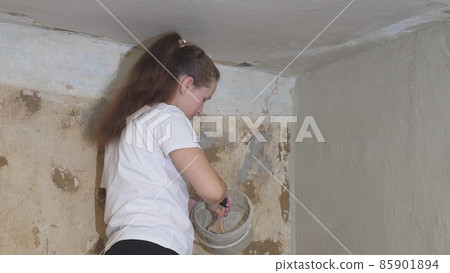 woman plasterer plasters the wall with brush, renovation work of an apartment, industrial construction contractor, cement work technology, finishing with dirty hand tool, build with concrete pavement 85901894