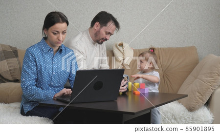 Mom is a freelancer working at the computer at home, the child and dad are playing with colorful cubes, the development of kid motor skills, family lifestyle, parents are raising a little daughter 85901895