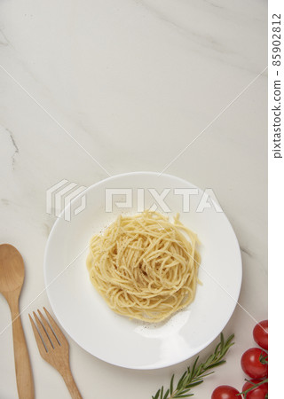pasta concept a dish of boiled long slim pasta being served on the white tile table together with a wooden spoon and fork, tiny red tomato, and other ingredients pasta concept a dish of boiled long slim pasta being served on the white tile table together with a wooden spoon and fork, tiny red tomato, and other ingredients 85902812