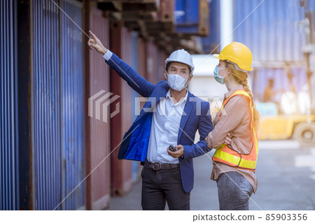 Manager and dock worker under discussion about dock container shipping warehouse document, they wearing safety uniform hard hat ,face mask and hold radio communication. 85903356