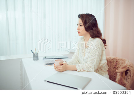 Asian female freelancer relaxing sitting with cup of coffee in front of laptop Asian female freelancer relaxing sitting with cup of coffee in front of laptop 85903394