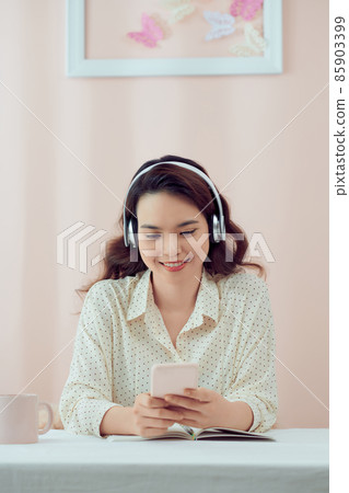 Happy woman at home wearing headphones watching videos on smart phone 85903399