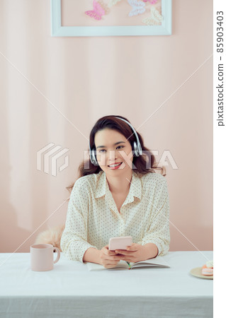 Image of serious beautiful woman using wireless headphones and cellphone while sitting at table Image of serious beautiful woman using wireless headphones and cellphone while sitting at table 85903403