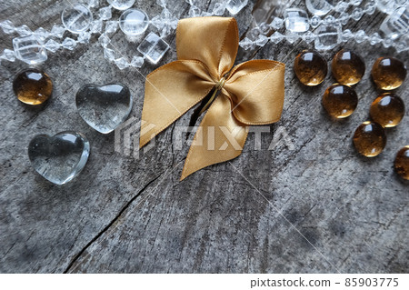 Shiny golden bow, transparent hearts and beads on the rough background of an old stump with a cleft Shiny golden bow, transparent hearts and beads on the rough background of an old stump with a cleft 85903775