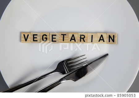 Top view white plate with vegetarian word against grey background top view, knife and fork on table health and food concept Top view white plate with vegetarian word against grey background top view, knife and fork on table health and food concept 85905053
