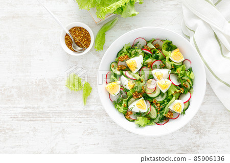 Easter fresh vegetable salad with boiled egg, radish and cucumber, dressing with dijon mustard and lemon on white wooden table. Top view Easter fresh vegetable salad with boiled egg, radish and cucumber, dressing with dijon mustard and lemon on white wooden table. Top view 85906136