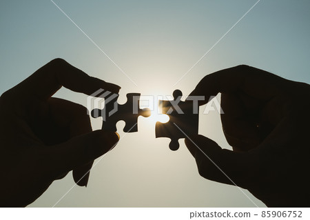 Silhouette of closeup woman and man hand connecting a piece of jigsaw puzzle over sunlight effect. symbol of association and connection concept. business strategy. Silhouette of closeup woman and man hand connecting a piece of jigsaw puzzle over sunlight effect. symbol of association and connection concept. business strategy. 85906752