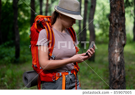 Young caucasian woman is hiking and using a compass in the forest. 85907005