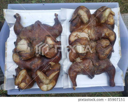 Delicious smoked chickens lies on a tray on foil. Delicious smoked chickens lies on a tray on foil. 85907151