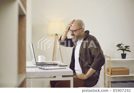 Argh, don't remember it. Middle aged or mature man slaps himself on face while working on laptop computer in home office. Businessman forgets password to his account or makes stupid mistake in project 85907292