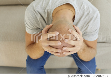 Stressed depressed man sitting alone on sofa, holding head in hands, thinking about mistakes, feeling lonely, desperate, devastated by life difficulties and adversities. Top view, close up, closeup 85907307