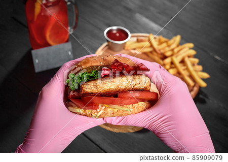 Hands in pink rubber gloves holding burger with pork steak, pickles, fresh vegetabels 85909079