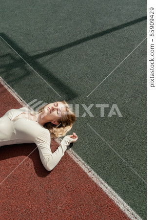 Young blonde female lying on a backetball sport field wih her eyes closed Young blonde female lying on a backetball sport field wih her eyes closed 85909429