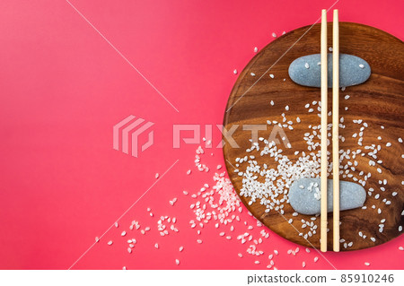 Chopsticks lie on oval stones and on a wooden surface on a pink background. 85910246