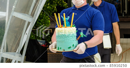 Waiters in gloves and masks carry on their hands a birthday cake with candles. Waiters in gloves and masks carry on their hands a birthday cake with candles. 85910250