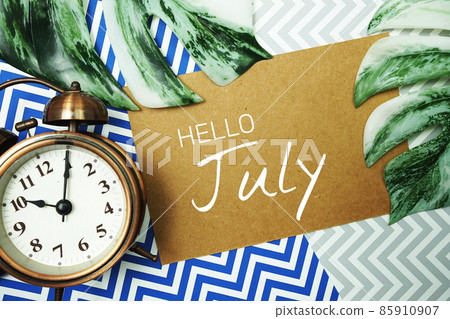 Hello July typography text on paper card with alarm clock and Monstera leave 85910907