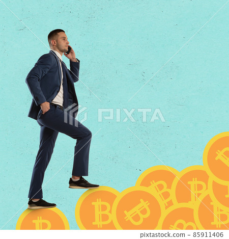 Increasing income. Young man, employee, stockbroker stepping on huge coins with bitcoin sign on blue background. Increasing income. Young man, employee, stockbroker stepping on huge coins with bitcoin sign on blue background. 85911406