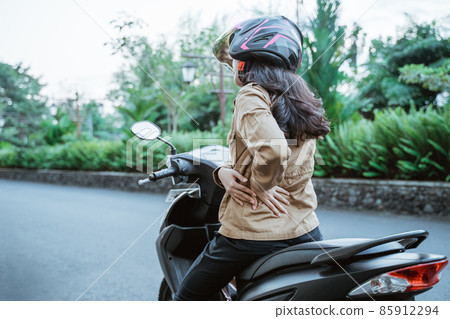 Woman wearing helmet stops riding motorbike due to back pain Woman wearing helmet stops riding motorbike due to back pain 85912294