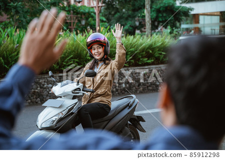 Woman wearing helmet riding motorbike waving with someone 85912298