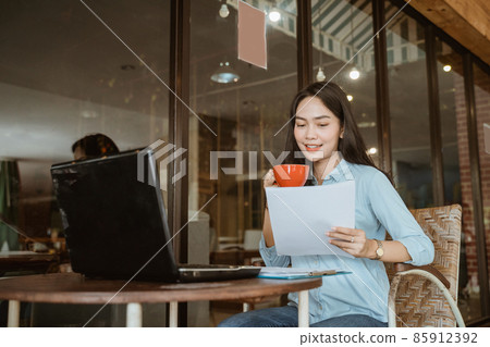 Asian woman holding coffee cup reading work paper Asian woman holding coffee cup reading work paper 85912392