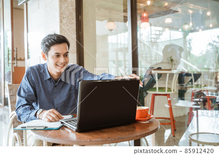 Asian man smiling while setting up laptop before online conference Asian man smiling while setting up laptop before online conference 85912420
