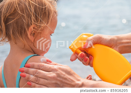 Mother applying sunscreen to her child at a beach 85916205