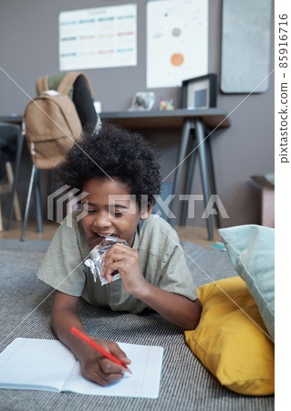 Cute African boy eating milk chocolate while drawing in copybook 85916716