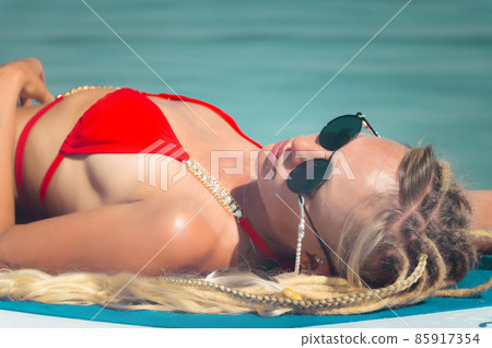An attractive Caucasian young woman in a red swimsuit and sunglasses lies and sunbathes on her paddle board while relaxing in the sea on the waves. Vacation at sea 85917354