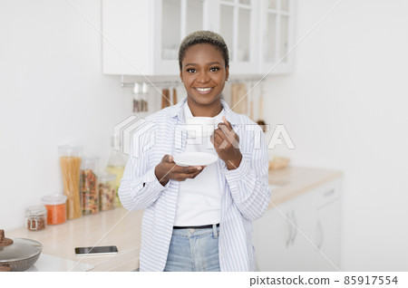 Cheerful pretty millennial black female in casual clothes drinking her favorite hot drink in white cup Cheerful pretty millennial black female in casual clothes drinking her favorite hot drink in white cup 85917554