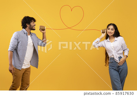 Love message. Loving indian man telling romantic words to girlfriend through tin can phone with heart shaped string 85917630