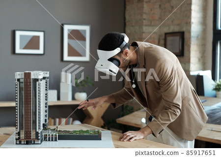 Young architect in vr headset bending over house layout Young architect in vr headset bending over house layout 85917651