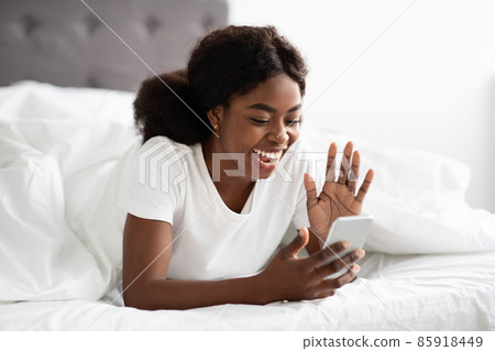 Happy african american woman laying in bed, having video call Happy african american woman laying in bed, having video call 85918449