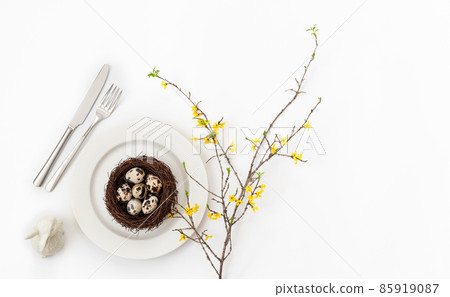Easter table setting with quail eggs in a nest , a branch of yellow forsythia flower and a rabbit on a white background. 85919087