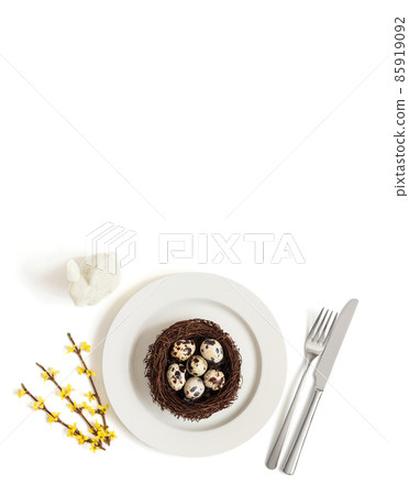 Spring Easter table setting with quail eggs in a nest on a plate, rabbit and yellow flowers on a white background. Vertical format. Copy space, top view 85919092
