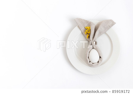 Easter table setting with egg in gray napkin Easter Bunny and a branch of yellow forsythia flowers on a white background. 85919172