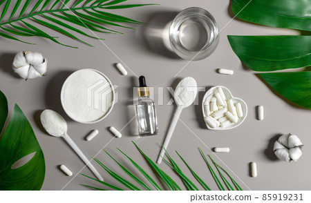 Set of collagen on a gray background with leaves. Collagen powder, capsules and liquid collagen. Natural supplement for skin beauty and bone health. View from above. 85919231