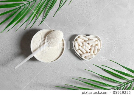 Collagen on a gray background with palm leaves. Collagen powder and pills. Fish or plant based supplement. Top view, flat lay. 85919235