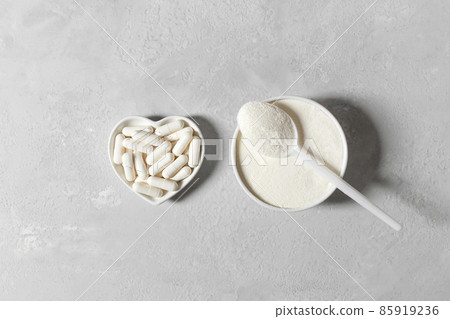 Collagen protein powder and pills on a gray background. A natural supplement for bone health and skin beauty. View from above. Collagen protein powder and pills on a gray background. A natural supplement for bone health and skin beauty. View from above. 85919236
