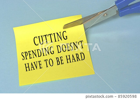 Scissors that cut yellow notepad with text on a blue background. Spending concept 85920598
