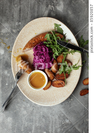 Grilled meat sausages and baked potatoes with vegetables on grey clay background Grilled meat sausages and baked potatoes with vegetables on grey clay background 85920857