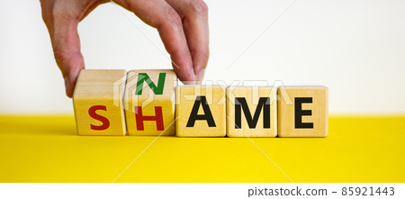 Name or shame symbol. Businessman turns wooden cubes and changes the word 'shame' to 'name' or vice versa. Beautiful yellow table, white background, copy space. Business, name or shame concept. Name or shame symbol. Businessman turns wooden cubes and changes the word 'shame' to 'name' or vice versa. Beautiful yellow table, white background, copy space. Business, name or shame concept. 85921443