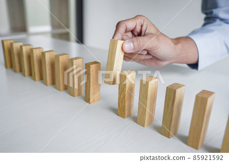 Risk and strategy in business, Close up of business woman hand gambling placing wooden block on a line of domino Risk and strategy in business, Close up of business woman hand gambling placing wooden block on a line of domino 85921592