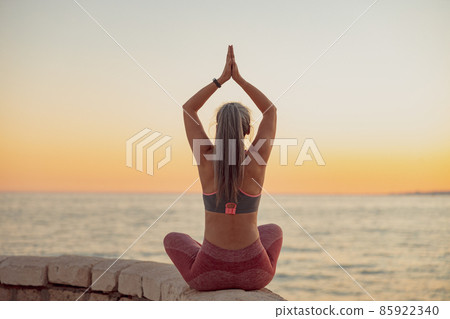 Mature woman in sportswear, sitting in lotus position on the edge of seafront 85922340