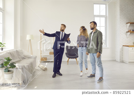 Realtor or real estate agent giving potential buyers or tenants tour about big house. Boyfriend and girlfriend or husband and wife who consider buying property looking at new modern spacious home 85922521