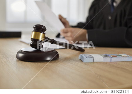 Law, auctioning, corruption, bankruptcy, bail, bribery or fines. Close up of judge gavel standing on sound block and bundle of dollars on table against background of judge or auctioneer with documents 85922524